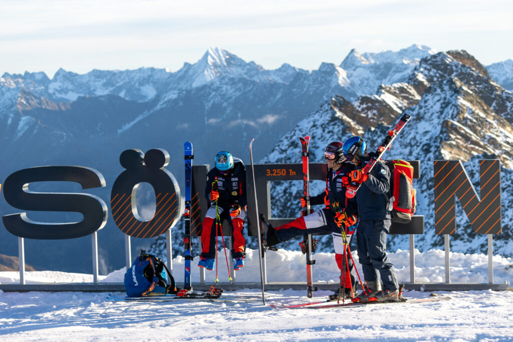 Skiers at Sölden ski resort resting next to the Sölden sign with mountains in the background.